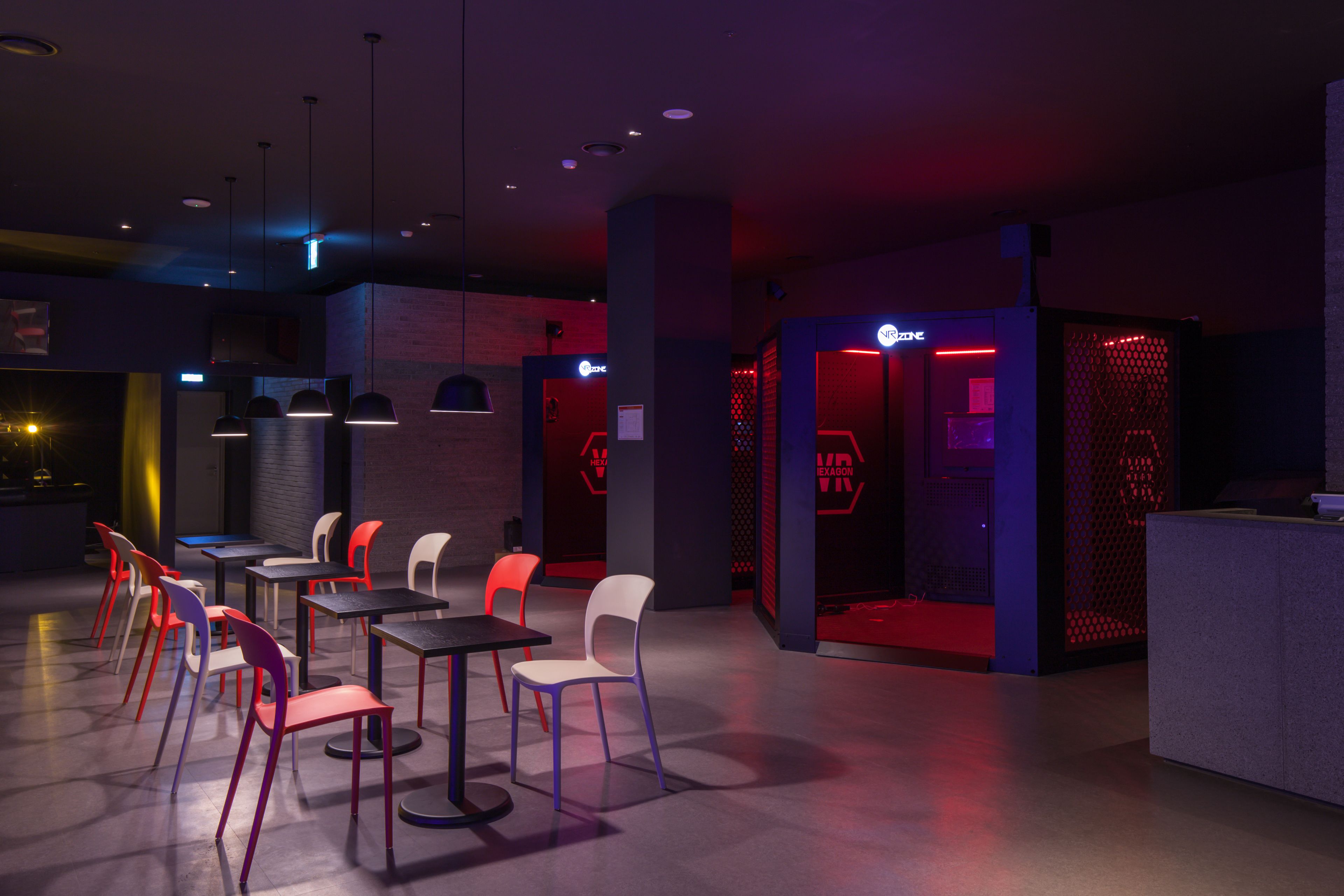 Un espacio interior moderno con mesas, sillas, una recepción y una pared con un logotipo.
