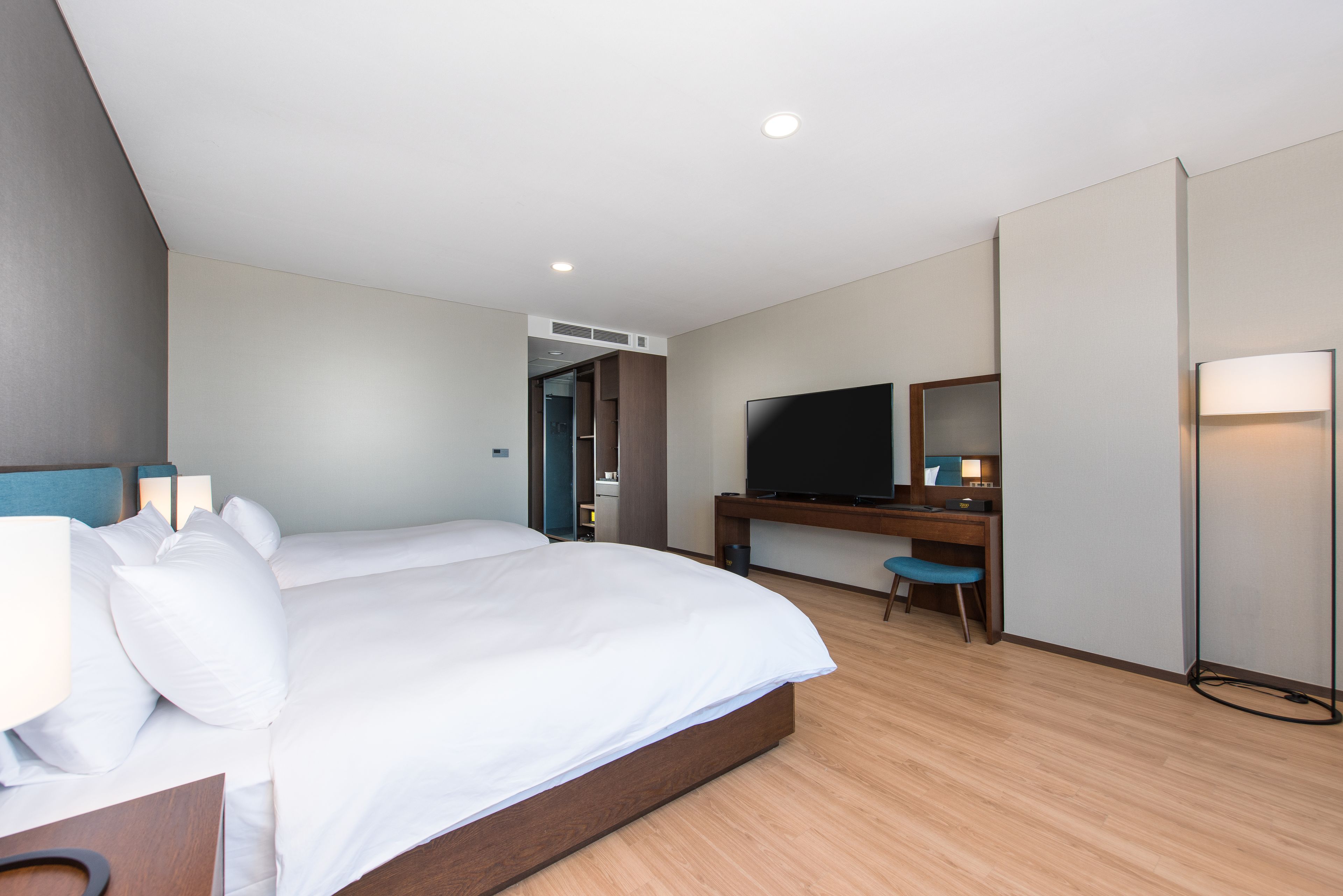 A modern hotel room with a large bed, a desk with a computer, a TV, and a bedside lamp.