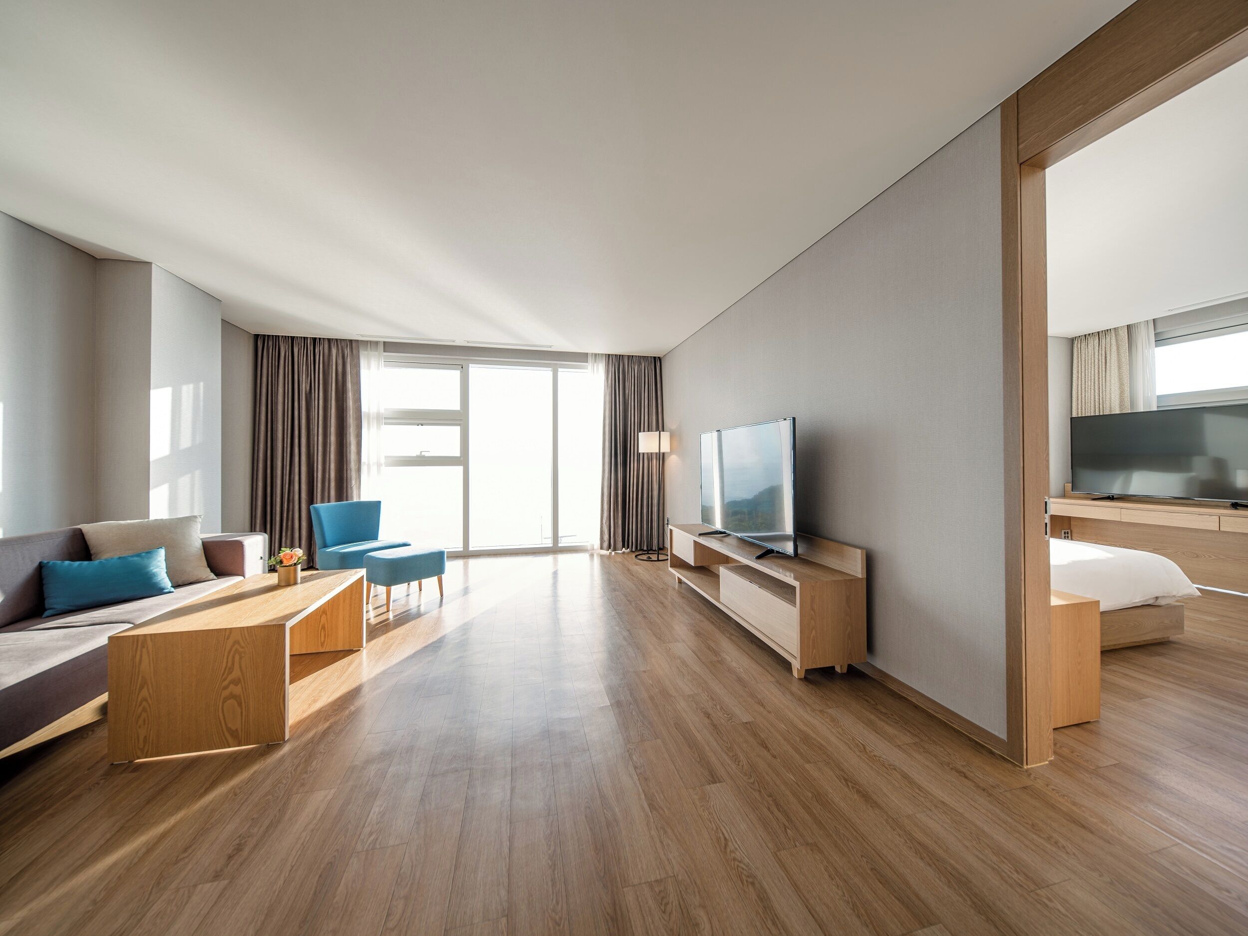 A modern hotel room with a large window, a flat-screen TV, a sofa, a coffee table, and a bed.