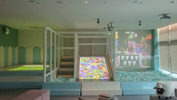 A children's play area with a slide, soft seating, and a projection screen displaying a colorful scene.