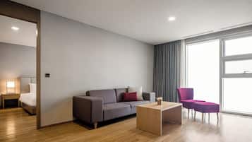Una habitación de hotel moderna con un sofá gris, una mesa de centro de madera y un sillón morado.
