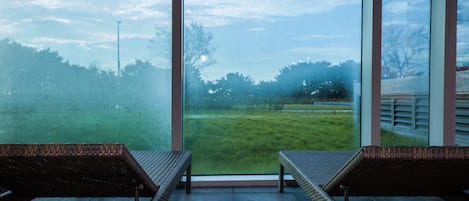 Una habitación con dos sillones de mimbre orientados hacia una ventana grande que da a un campo cubierto de hierba.