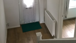 A staircase with a green mat at the bottom, a white door with a window, and a white radiator on the wall. - Nice 4 Bedroom near Basildon Town Center (Basildon)