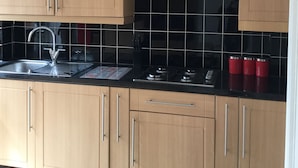 A kitchen with wooden cabinets, a stainless steel sink, black tiled backsplash, and a gas stove. - Nice 4 Bedroom near Basildon Town Center (Basildon)