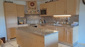 A kitchen with wooden cabinets, a granite countertop, and a built-in microwave. - Appartement Esserts A14 (Val d'Illiez)
