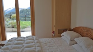 A bedroom with a bed, a wooden headboard, and a view of a mountain landscape through a glass door. - Appartement Esserts A14 (Val d'Illiez)