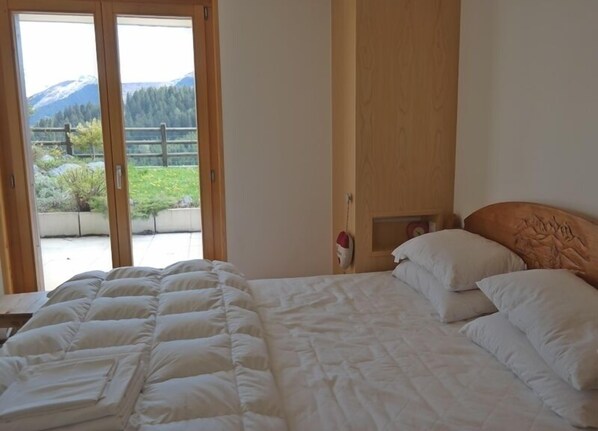 A bedroom with a bed, a wooden headboard, and a view of a mountain landscape through a glass door.