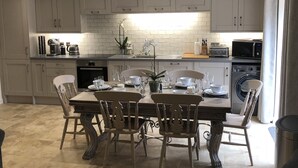 A modern kitchen with white cabinets, a dining table set for four, and a washing machine. - Camerton Inn Cottage (Bath)