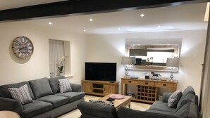 A modern living room with a grey sofa set, a flat-screen TV, a wooden coffee table, and a small side table with a lamp. - Camerton Inn Cottage (Bath)