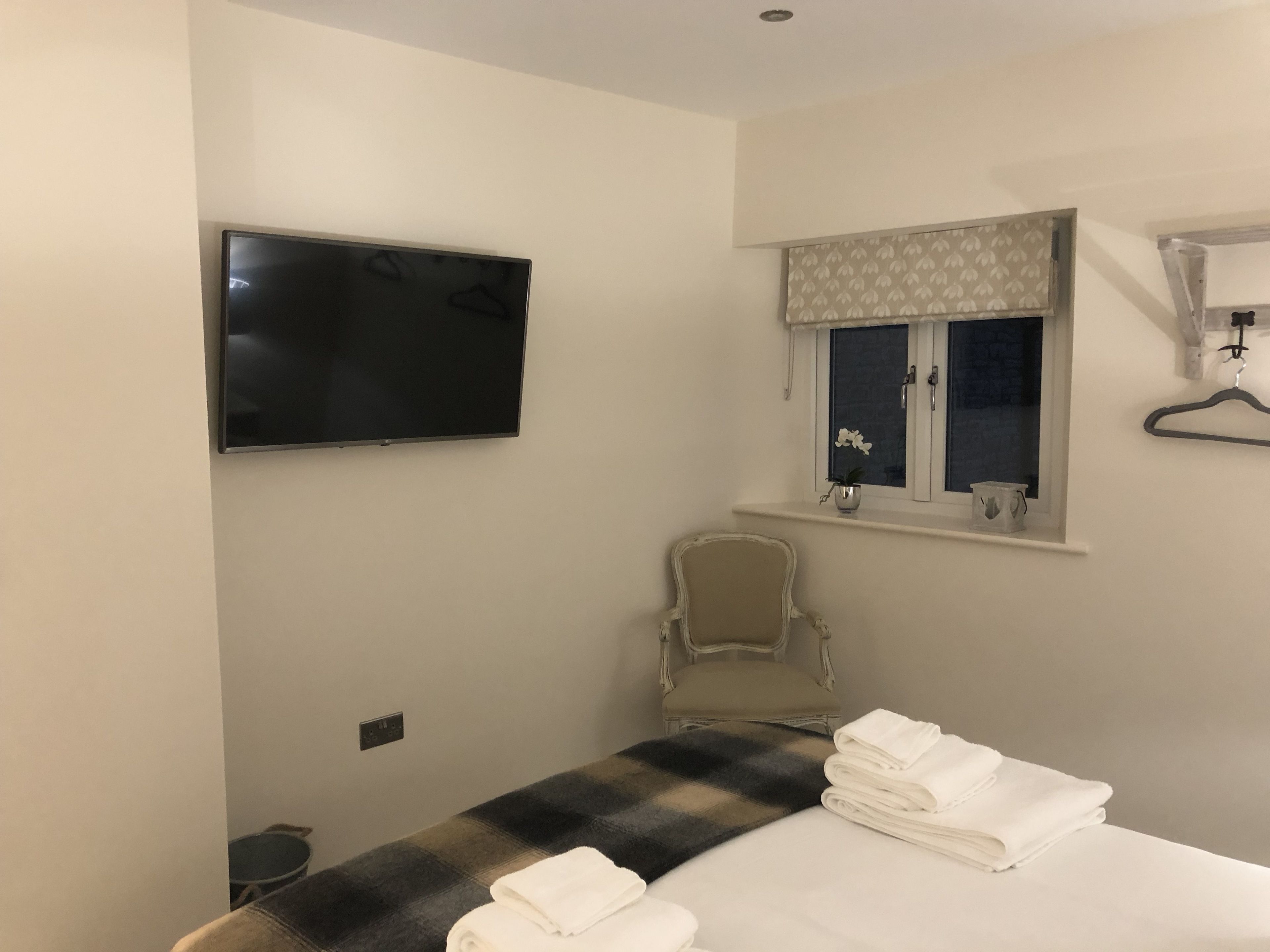 A hotel room with a bed, a chair, a television, a window with curtains, and a small table with towels.