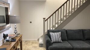 A living room with a grey sofa, a wooden coffee table, a lamp, and a staircase. - Camerton Inn Cottage (Bath)
