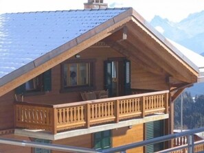 A wooden chalet with a balcony, a chimney, and a mountain backdrop. - Appartement Esserts A42 (Val d'Illiez)
