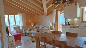 A cozy living room with a wooden ceiling, a dining area with a wooden table and chairs, and a kitchen with white cabinets. - Appartement Esserts A42 (Val d'Illiez)