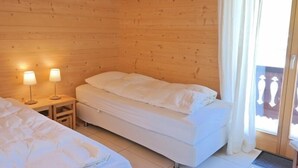 A wooden cabin room with two beds, a nightstand with lamps, and a window with curtains. - Appartement Esserts A42 (Val d'Illiez)
