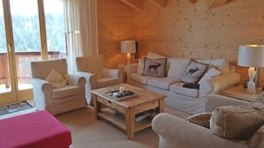 A cozy wooden cabin interior with a sofa set, two armchairs, a coffee table, and a red ottoman. - Appartement Esserts A42 (Val d'Illiez)