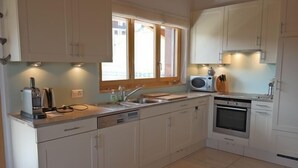 A compact kitchen with white cabinets, a built-in oven, a sink, and a window providing natural light. - Appartement Esserts A42 (Val d'Illiez)