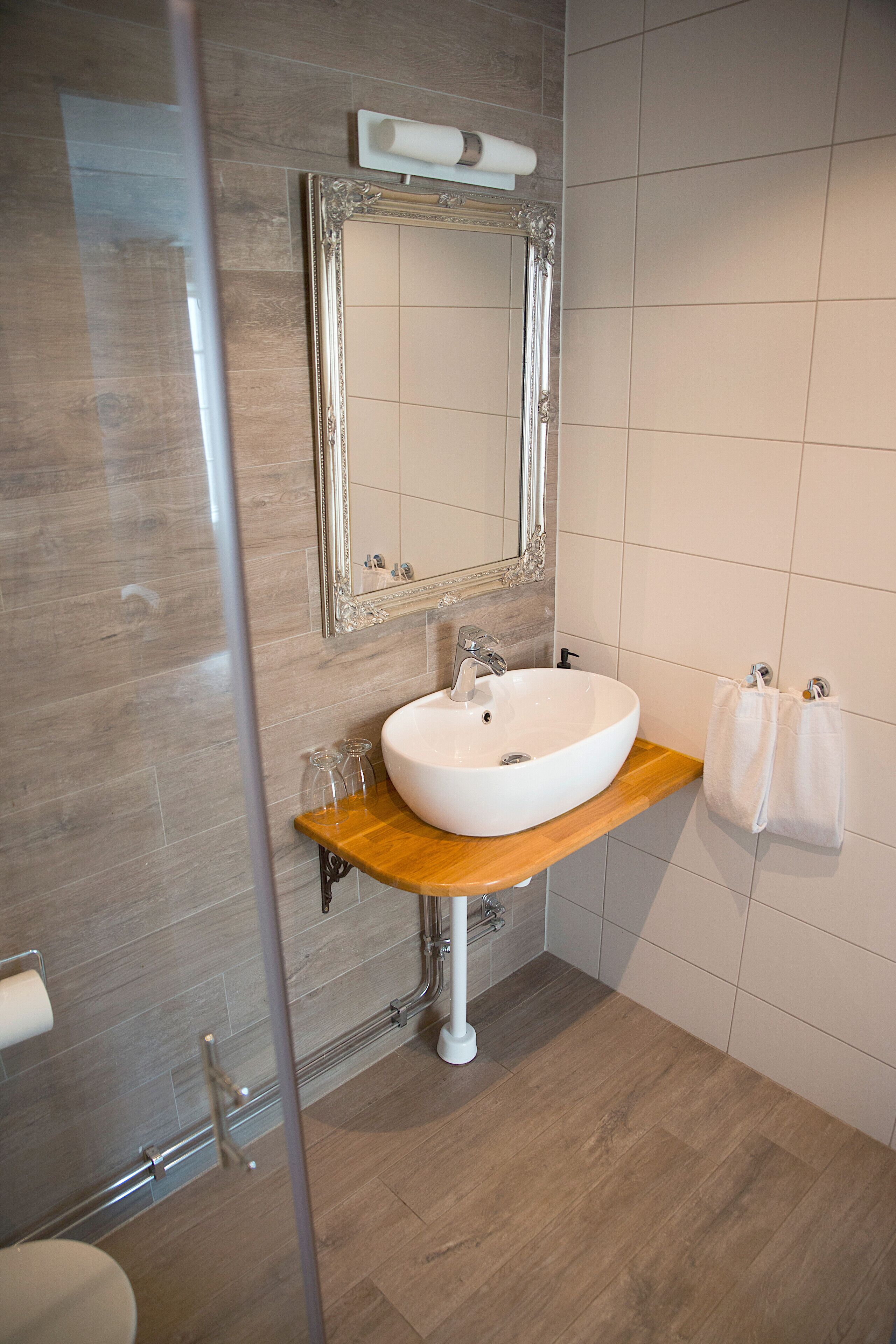 Un baño con tocador de madera, un lavabo blanco, un espejo con marco decorativo y un perchero para toallas.