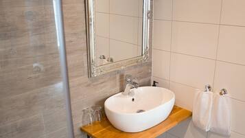 Un baño con tocador de madera, un lavabo blanco, un espejo con marco decorativo y un perchero para toallas.