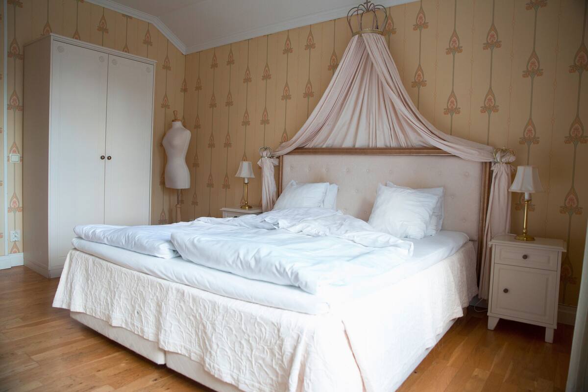 Ein ordentlich bezogenes Bett mit Baldachin, ein Kleiderschrank und Nachttischlampen in einem Hotelzimmer.