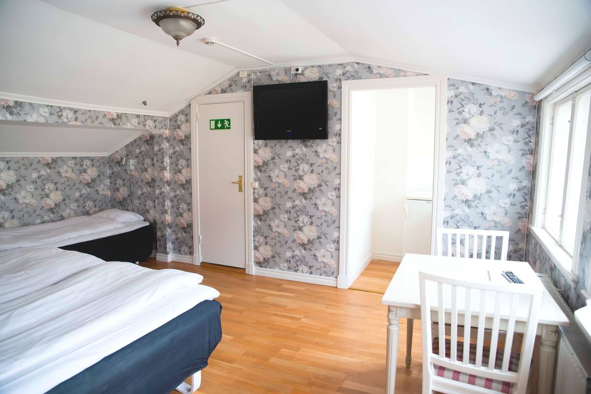 Ein Zimmer mit zwei Betten, einem Tisch und einem Fernseher.