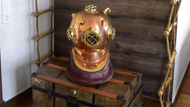 Una habitación con una escalera de cuerda, un modelo de submarino de cobre y un cofre de madera.