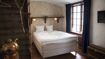 A bed with white linens, a wooden headboard, and a window with curtains.
