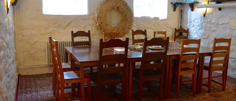 A dining area with a round table, wooden chairs, a patterned rug, a decorative wreath, and a stone wall.