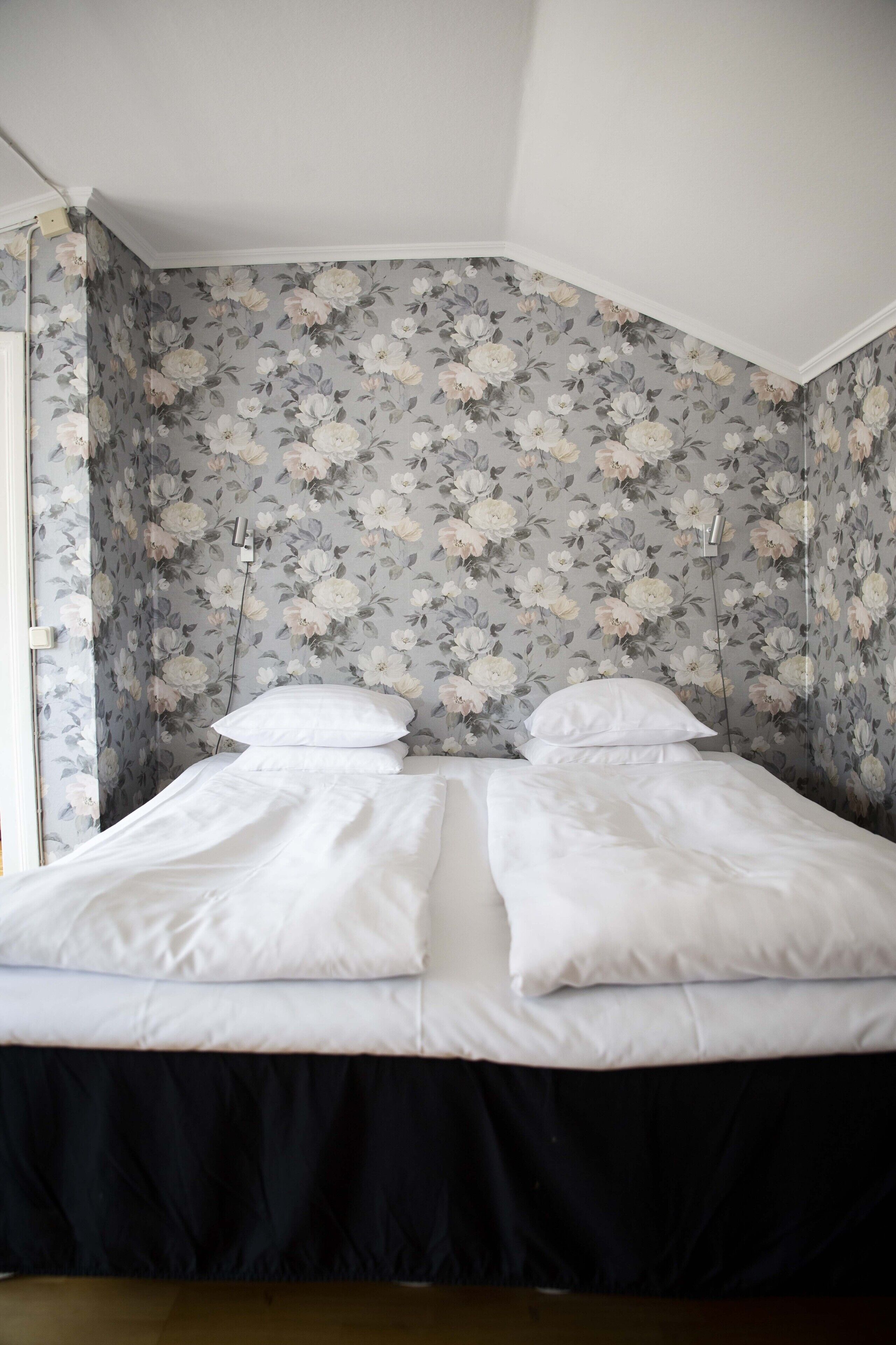 Un dormitorio con papel tapiz floral, una cama con ropa de cama blanca y un cabecero negro con falda.
