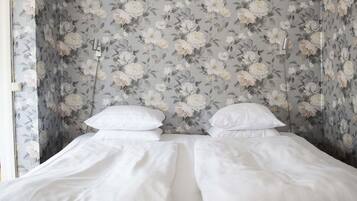 Un dormitorio con papel tapiz floral, una cama con ropa de cama blanca y un cabecero negro con falda.