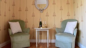 Dos sillones verdes con cojines blancos, una mesita pequeña con una botella y vasos, y un espejo en la pared.
