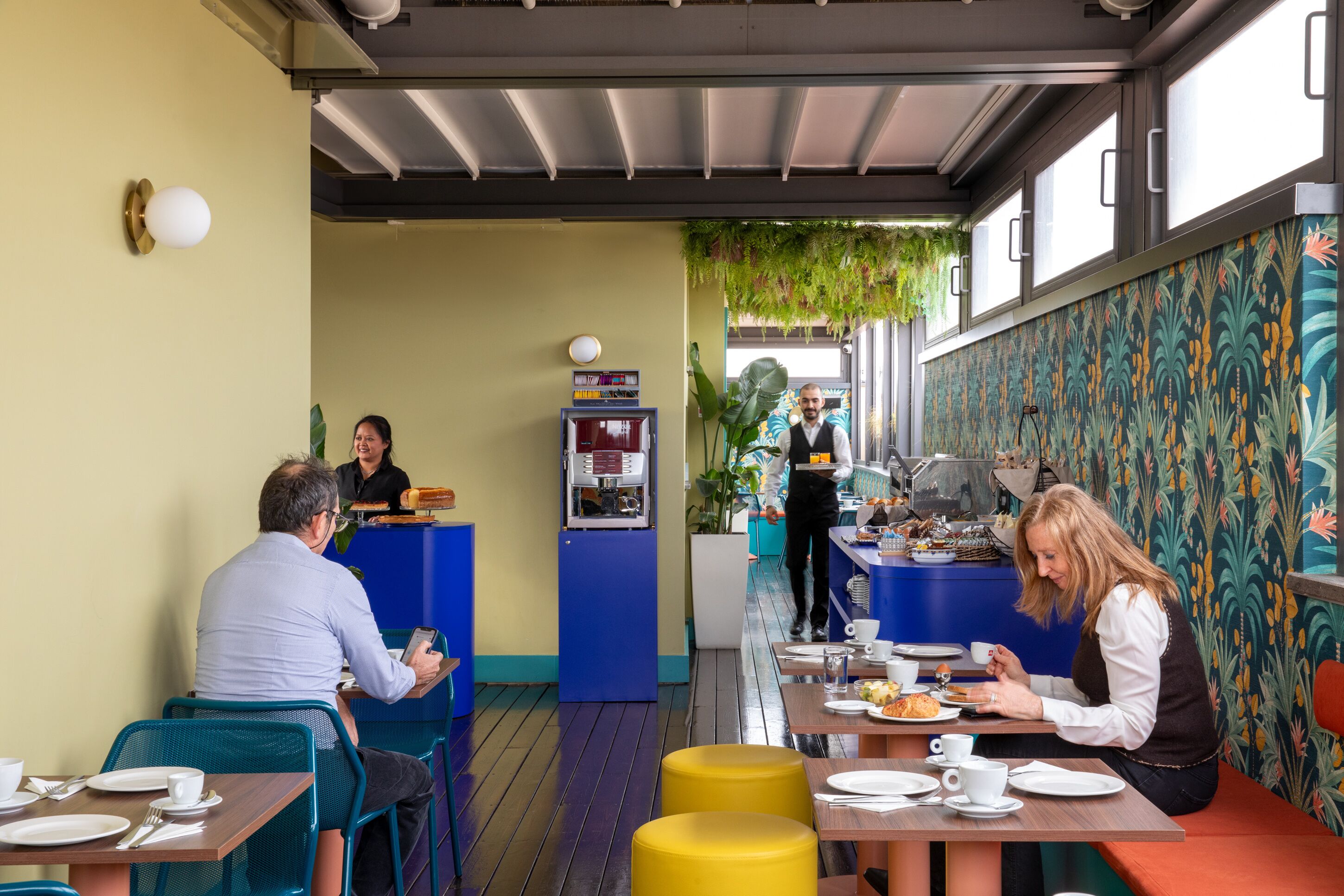 A restaurant with tables and chairs, a counter with a server, and a coffee machine.