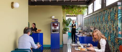 A restaurant with tables and chairs, a counter with a server, and a coffee machine.