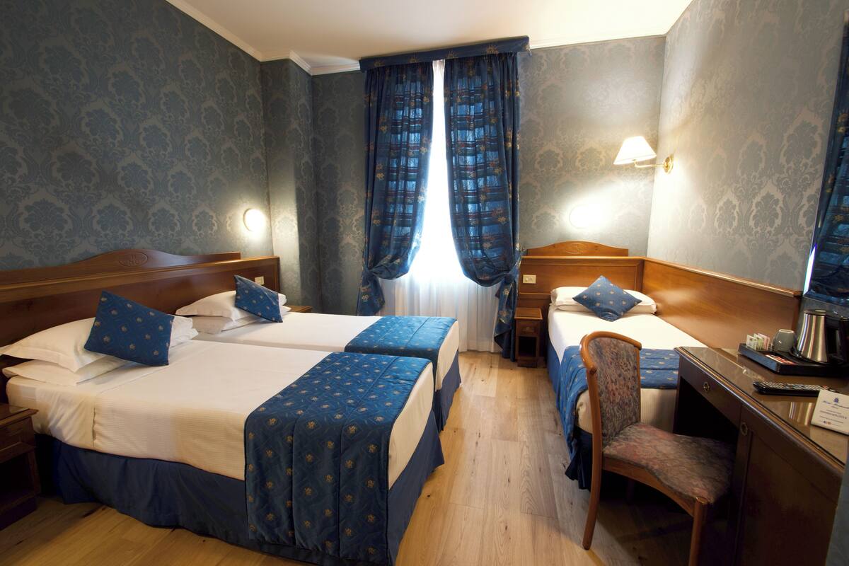 Una camera d'albergo con due letti, una scrivania, una sedia e un comodino.