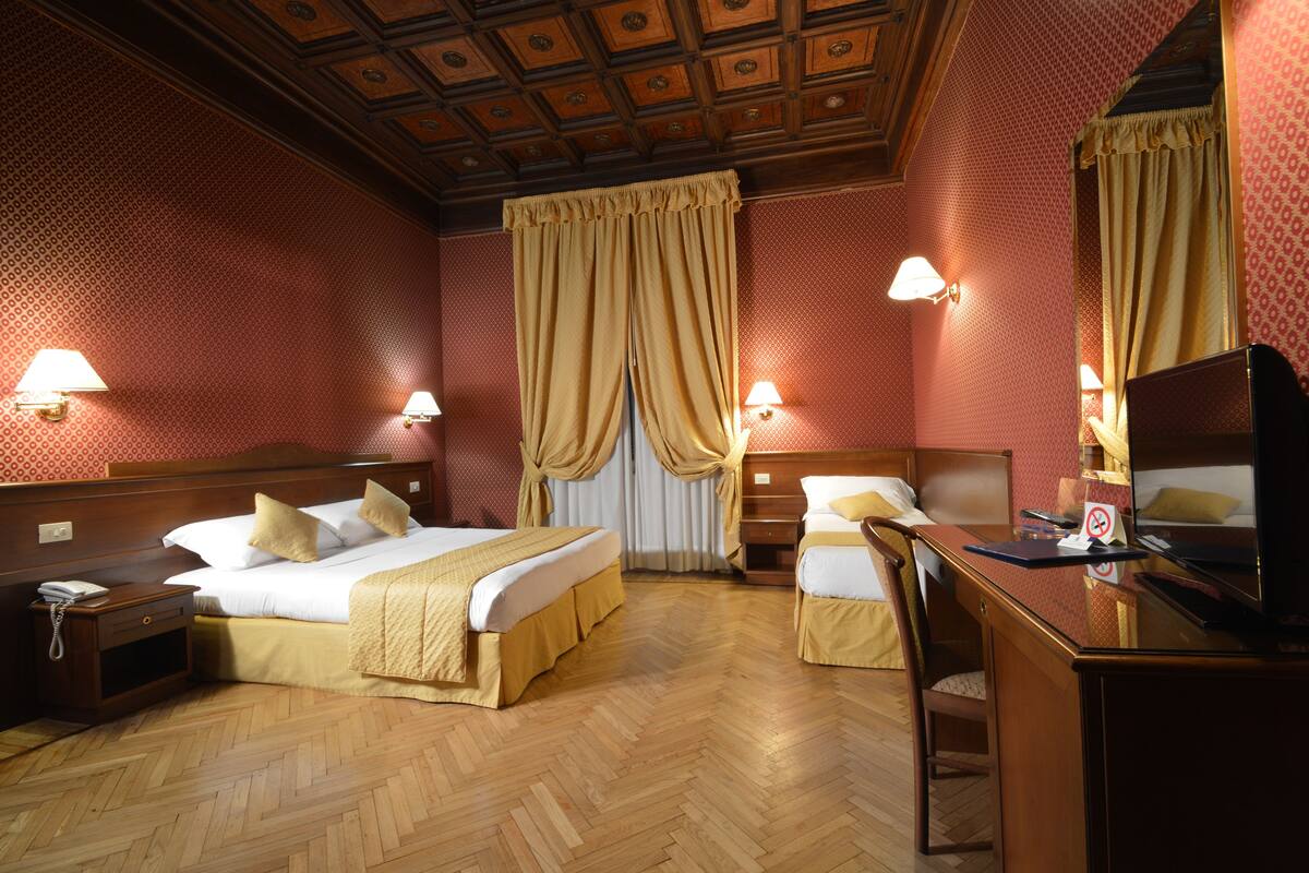 Una camera d'albergo con pavimento in legno, due letti, una scrivania e un televisore.
