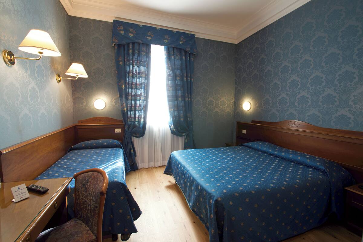 Camera d'albergo con due letti singoli, una scrivania con una sedia e due lampade a parete.