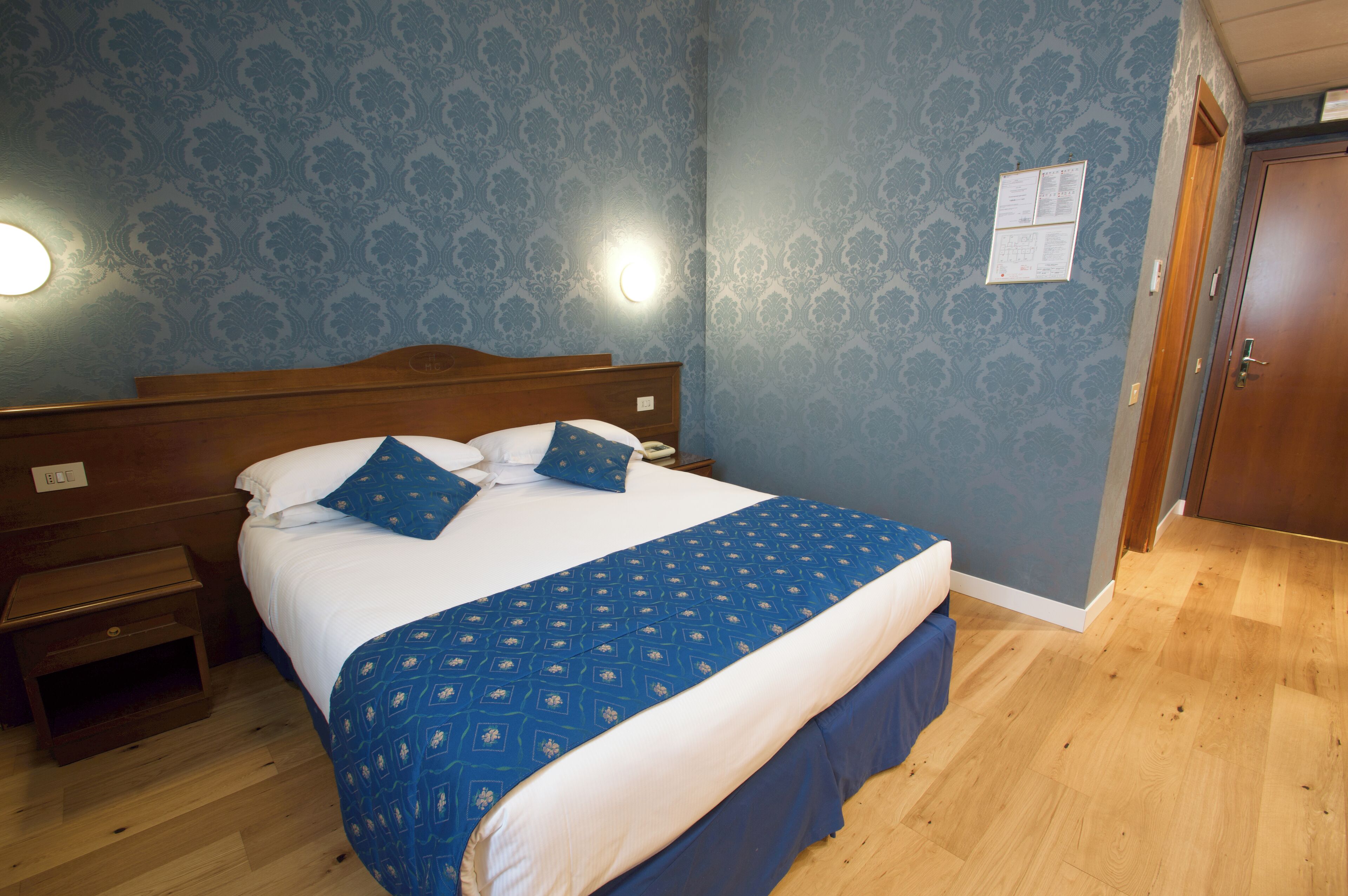 A neatly made bed with a blue and white bedspread, a wooden headboard, and a nightstand with a lamp.