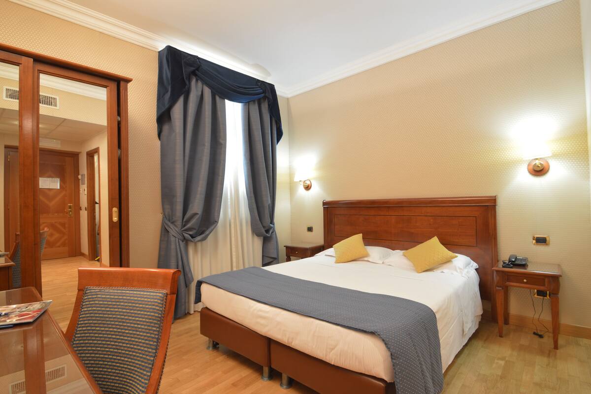 Una camera d'hotel con un letto di legno, un comodino, una sedia e una scrivania con una lampada.