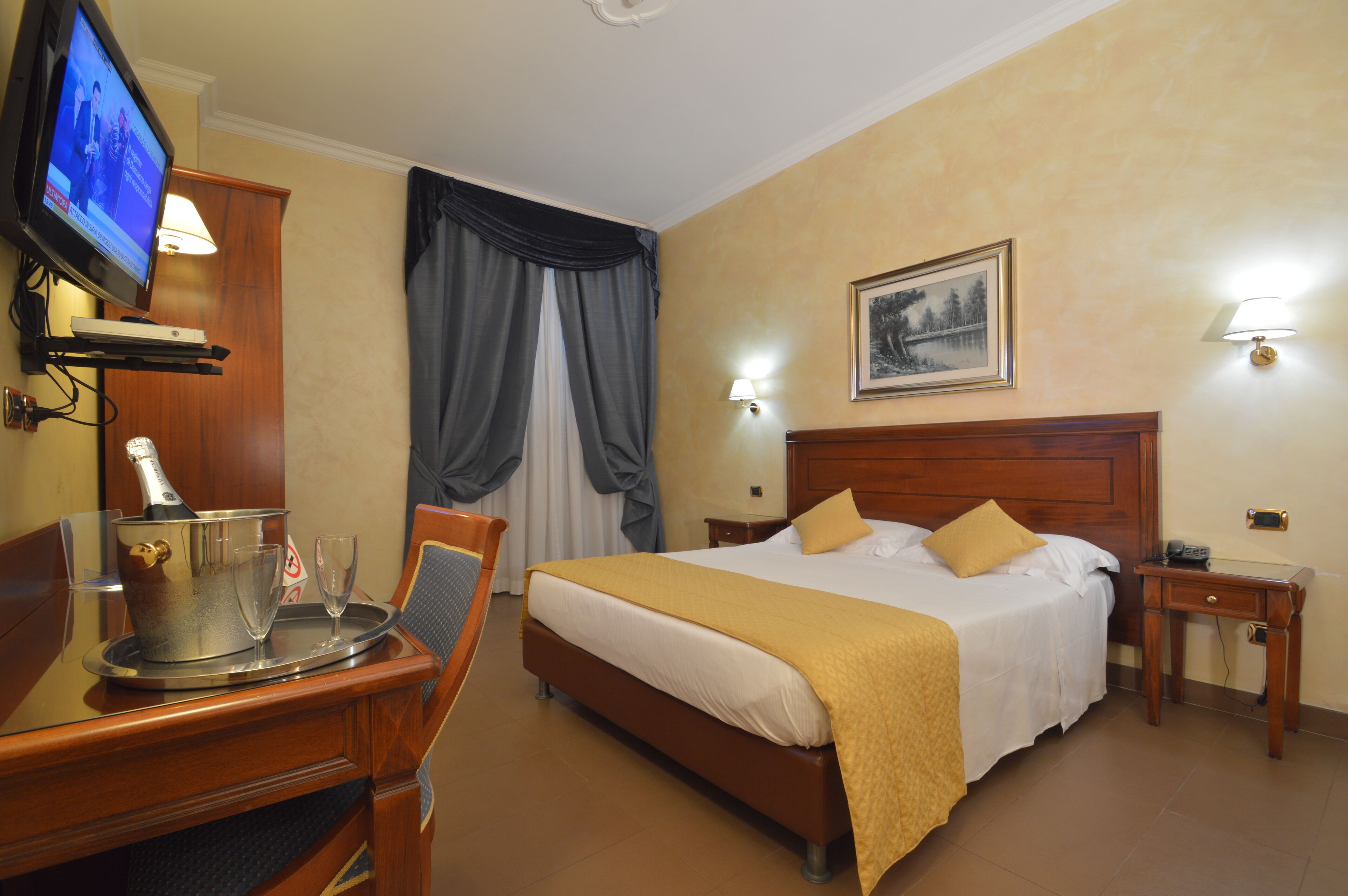 A hotel room with a bed, a TV, a bedside table, a lamp, and a picture on the wall.