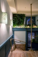 Una escalera con barandilla, un aplique de pared y una pared verde con plantas.