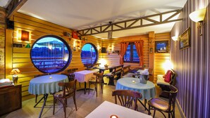 Un restaurant chaleureux avec des murs en bois, des tables rondes et de grandes fenêtres offrant une vue panoramique.