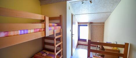 A dormitory room with bunk beds, a wooden desk, and a window providing natural light.