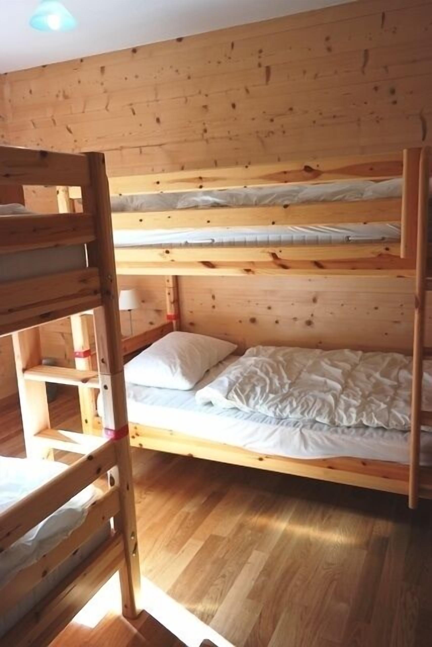 Una camera con letto a castello, pareti e pavimento in legno, una lampada da comodino e un piccolo ripiano.