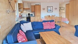 A compact living space with a blue sofa, a wooden dining table, and a kitchenette. - Appartement Esserts A33 (Val d'Illiez)