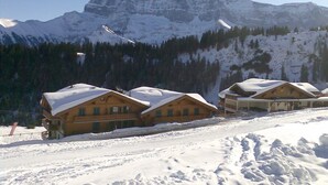 A snow-covered mountain lodge with wooden cabins, a ski slope, and a clear view of the surrounding peaks. - Appartement Esserts A33 (Val d'Illiez)