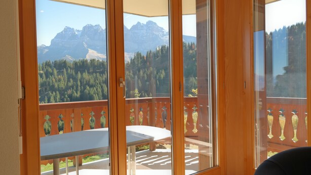 A balcony with a table and chairs, offering a view of a mountainous landscape. - Appartement Esserts A33 (Val d'Illiez)