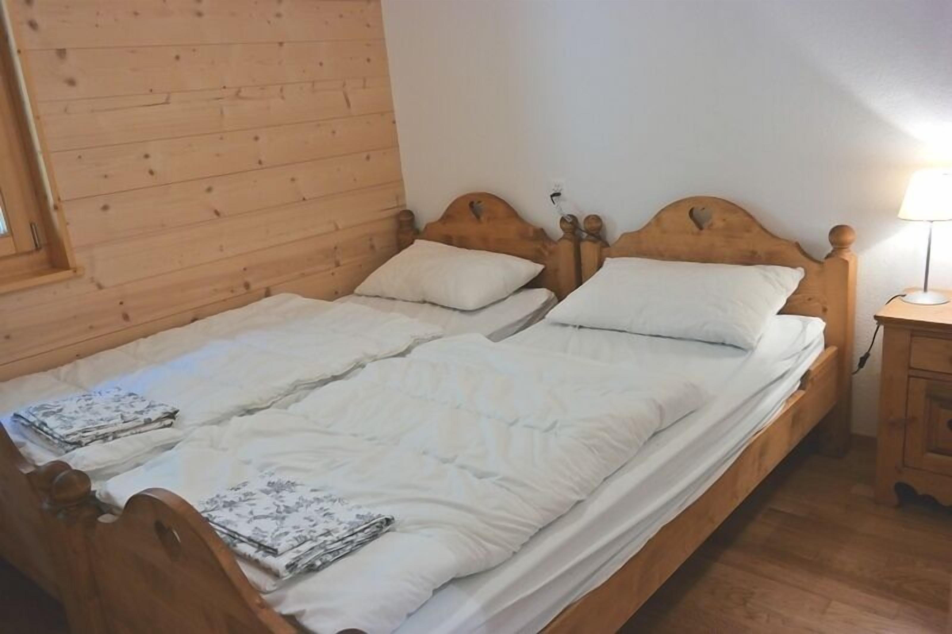 Cama doble con cabecera y piecera de madera, ropa de cama blanca y una mesita de noche con lámpara.