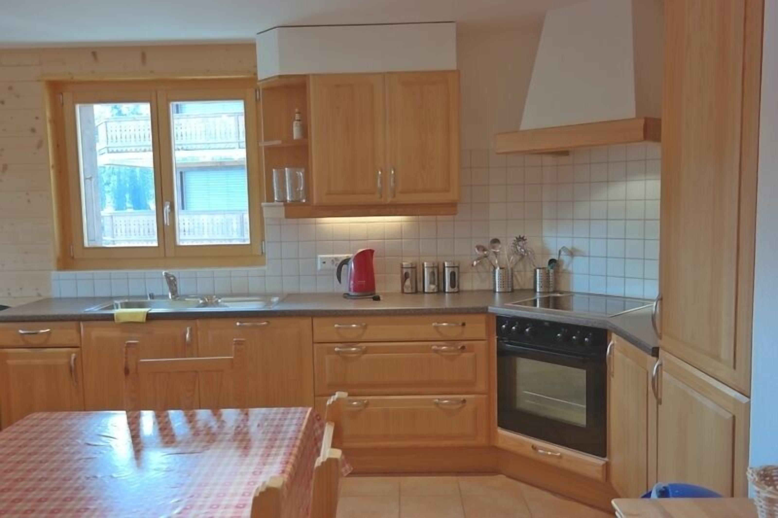 Une cuisine avec des meubles de rangement en bois, une cuisinière et une fenêtre donnant sur des immeubles.