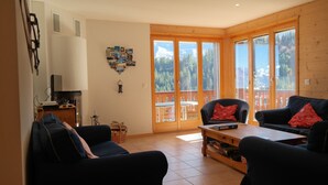 A cozy living room with a fireplace, a coffee table, and two sofas with red cushions. - Appartement Esserts A33 (Val d'Illiez)