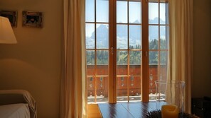 Una habitación con un ventanal grande, una cama, una mesa con una vela y cuadros en la pared.
