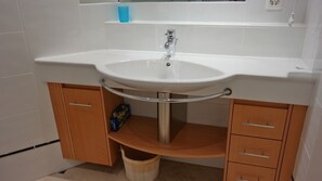 Ein Badezimmer mit einem weißen Waschbecken, Holzschränken und einer blauen Tasse auf der Ablagefläche.